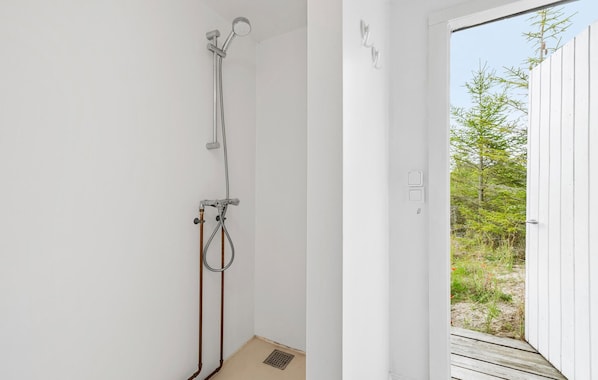 A bathroom with a shower, a toilet, and a sink. There is a window with a view of trees and a wooden deck outside.