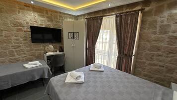 A hotel room with two beds, a desk, a TV, and stone walls.