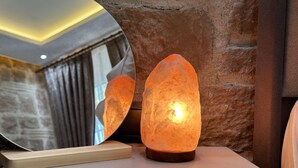 Eine Salzlampen auf einem Holzständer, mit einem Spiegel, der einen Raum mit Steinwänden und einem mit Vorhängen drapierten Fenster zeigt.