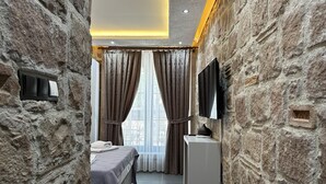 Ein Schlafzimmer mit Stehwänden, einem Bett, einem Nachttisch, einem Fernseher und einem Fenster mit Vorhängen.