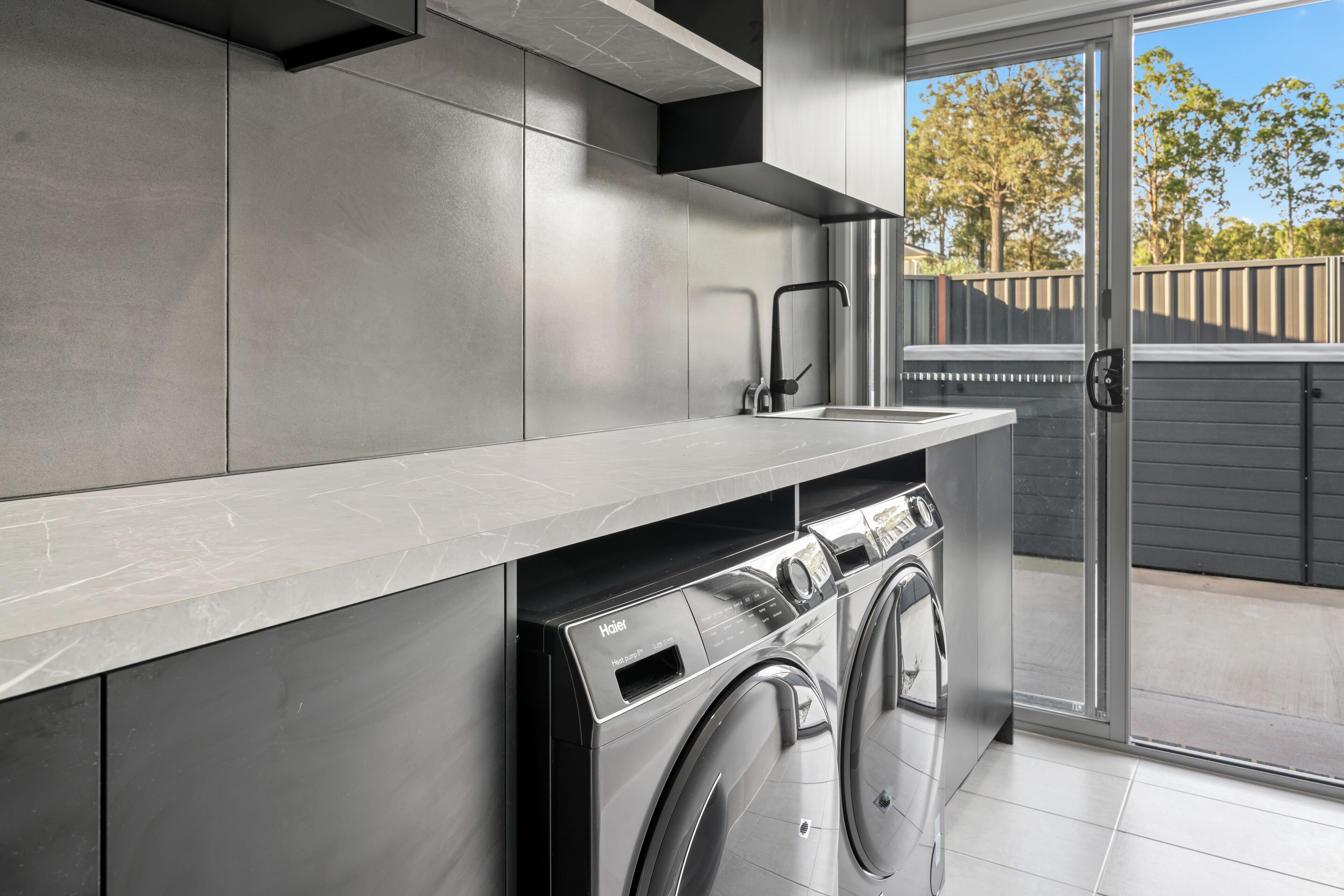A modern kitchen with a built-in washer and dryer, a large window, and a sliding glass door leading to a balcony.