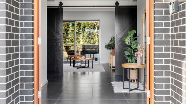 A modern hallway with a brick wall, a wooden door frame, and a view into a dining area with a table and chairs. - Serenity Estate Hunter Valley (Millfield)