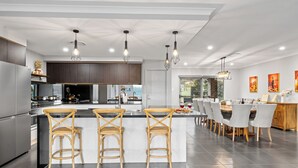 A modern kitchen with a central island, bar stools, and pendant lighting. - Serenity Estate Hunter Valley (Millfield)
