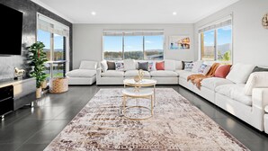 A modern living room with a sectional sofa, a round coffee table, and a large window offering a scenic view. - Serenity Estate Hunter Valley (Millfield)
