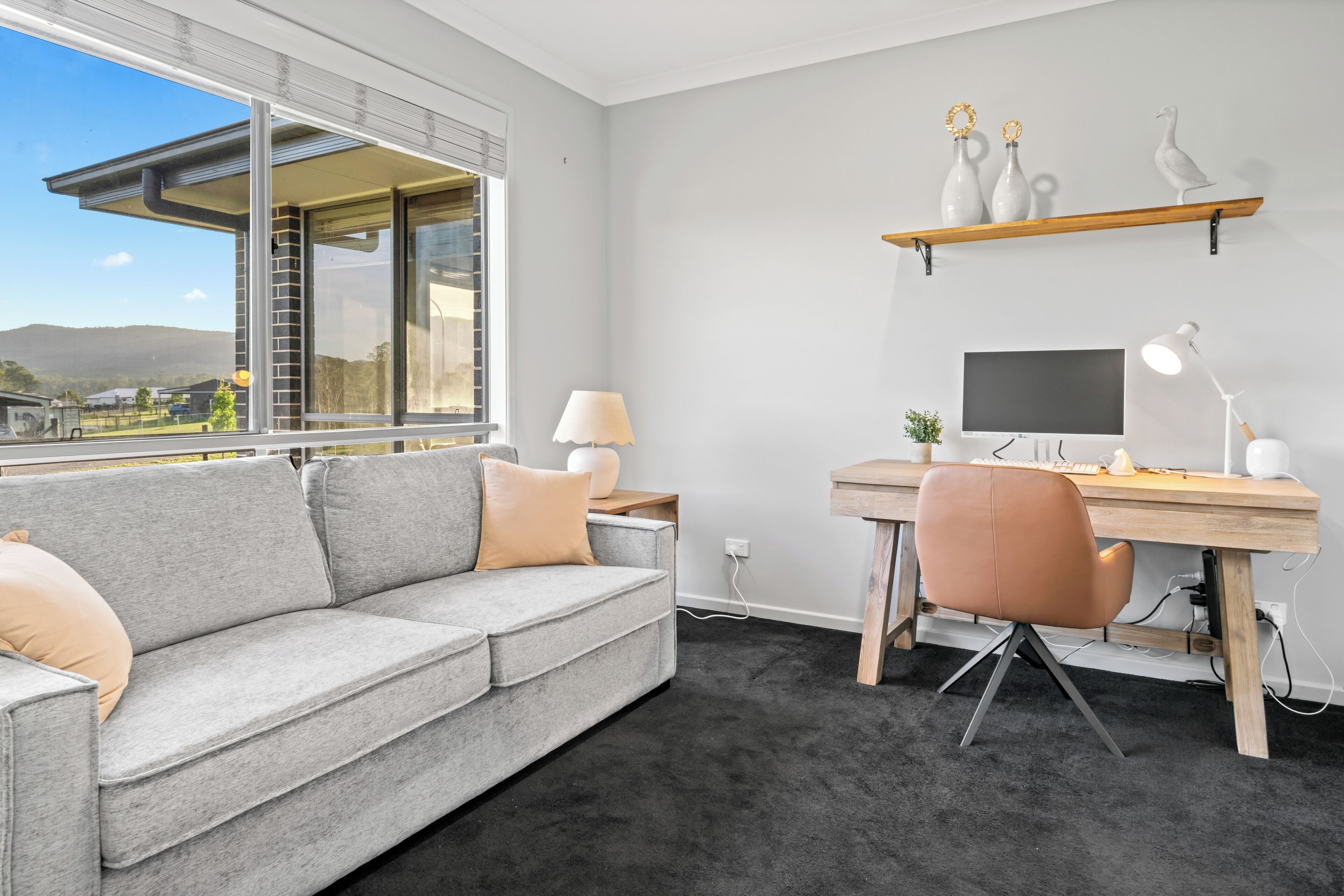 Un salon moderne avec un canapé gris, un bureau en bois, un ordinateur et un téléviseur.