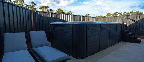 An outdoor hot tub area with lounge chairs and a staircase leading to a deck.
