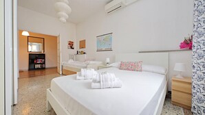 Une chambre d’hôtel avec un grand lit, une table de chevet avec une lampe, un petit bureau avec une chaise, un miroir, une carte accrochée au mur et une fenêtre avec un rideau.