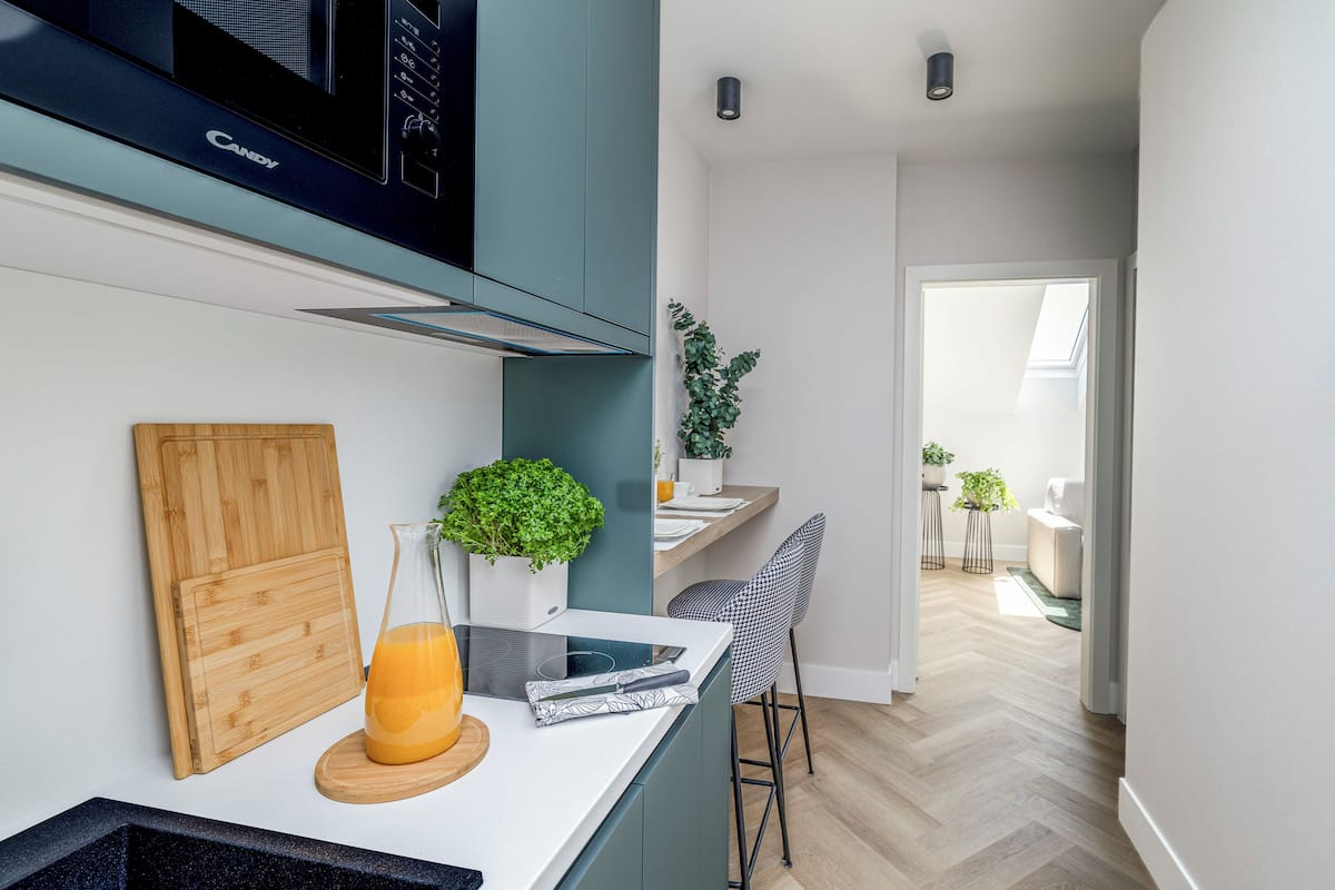 A modern kitchen with a built-in microwave, a wooden cutting board, a glass pitcher of orange juice, and a tablet on the counter.
