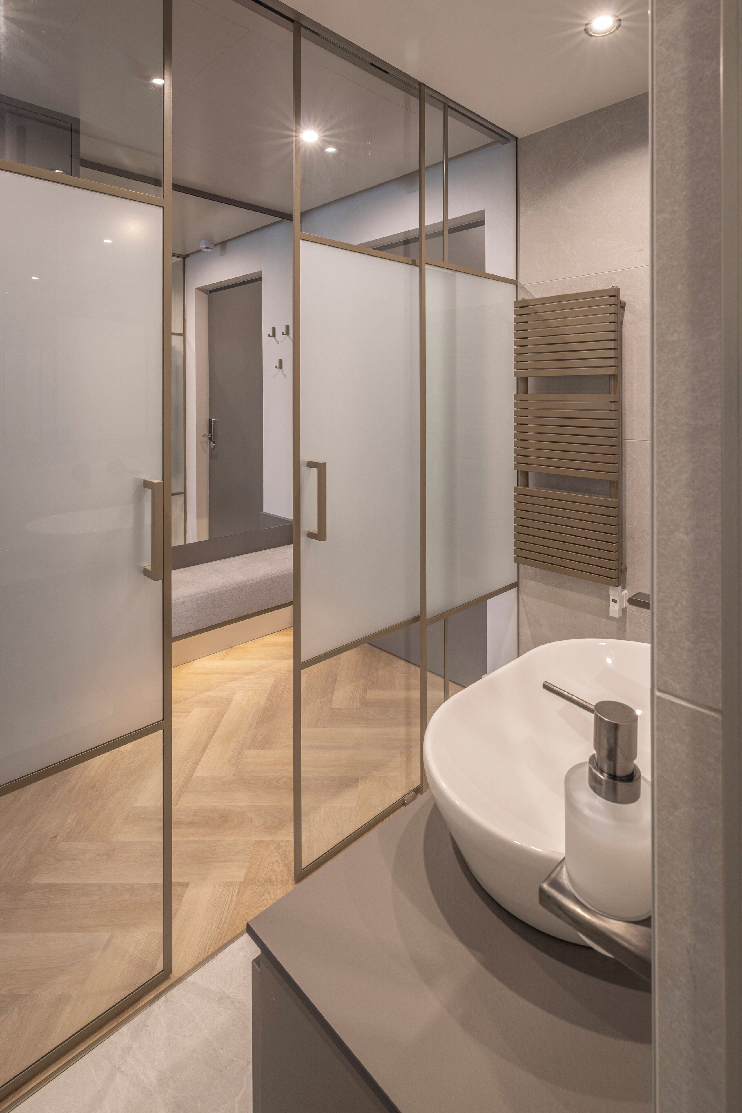 A modern bathroom with a glass partition, a white sink, and a wooden floor.