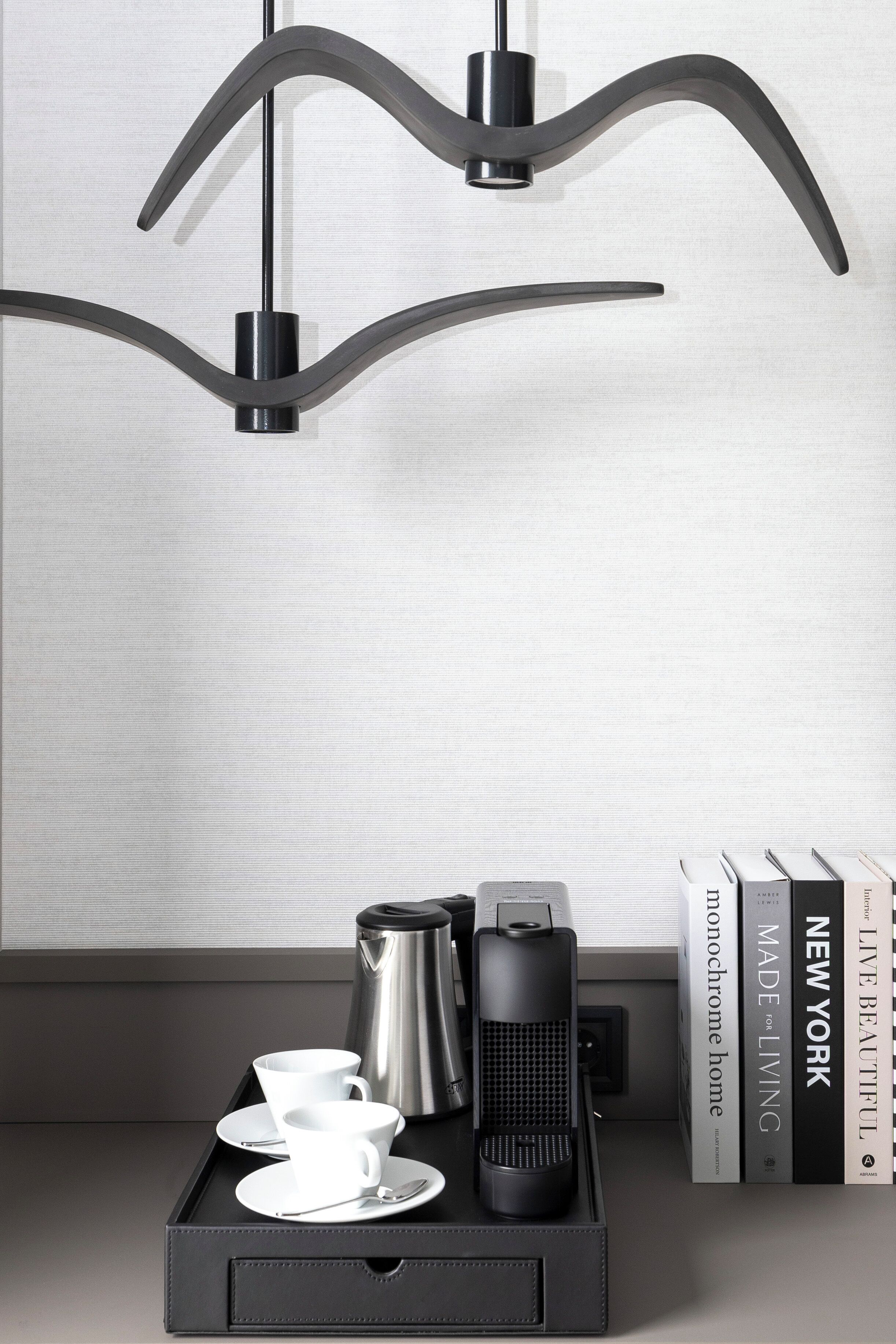 Un interior moderno con diseño minimalista, que presenta una bandeja negra con una cafetera, tazas y un control remoto, junto con una colección de libros en una estantería.