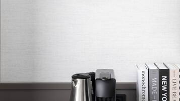 Un interior moderno con diseño minimalista, que presenta una bandeja negra con una cafetera, tazas y un control remoto, junto con una colección de libros en una estantería.