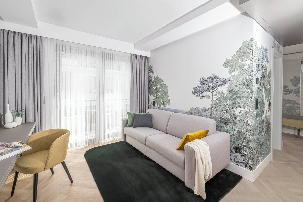 A modern living room with a sofa, a chair, and a large window with sheer curtains.