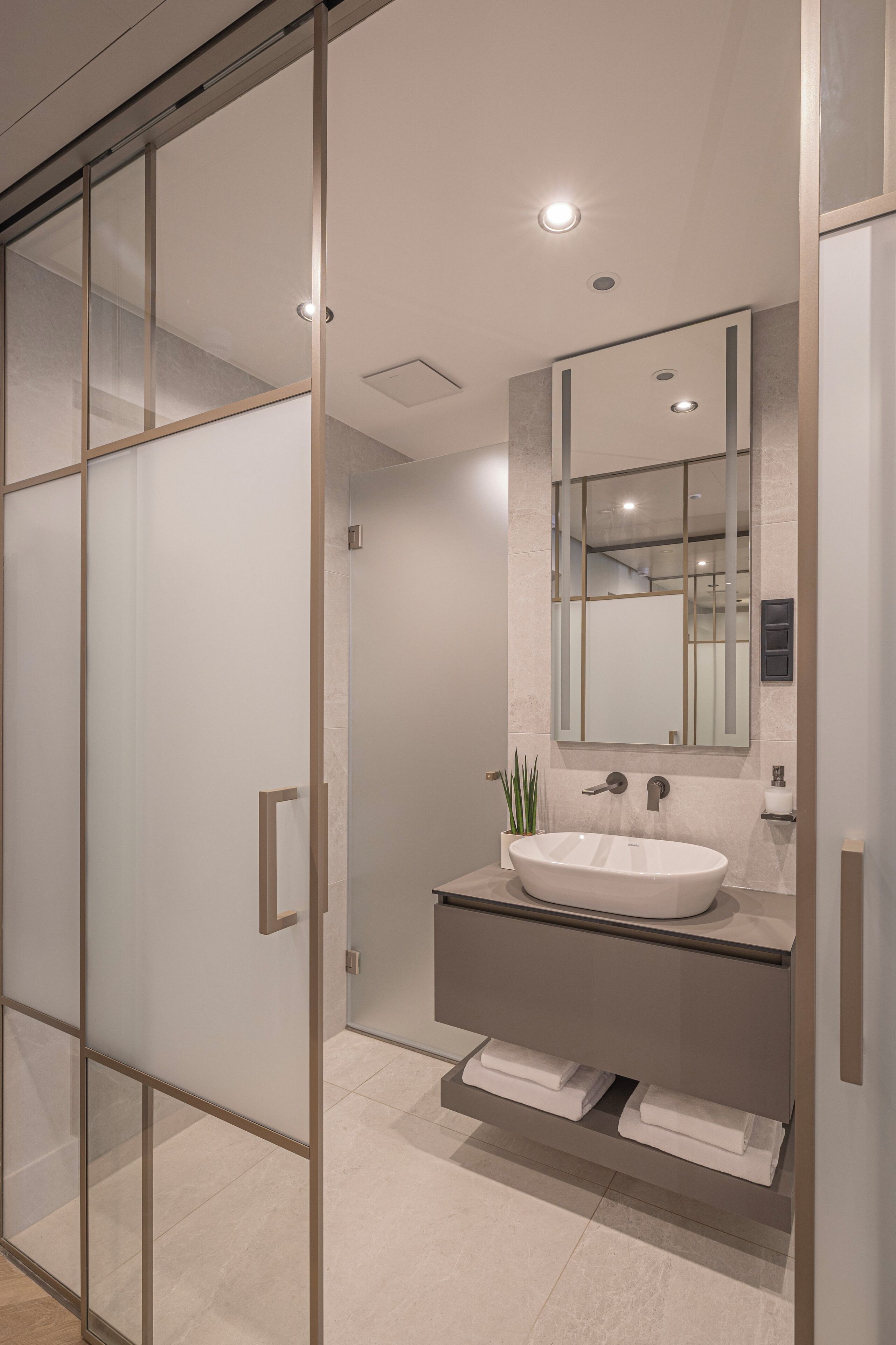 Un baño moderno con cabina de ducha de vidrio, un lavamanos blanco con espejo y un perchero para toallas.
