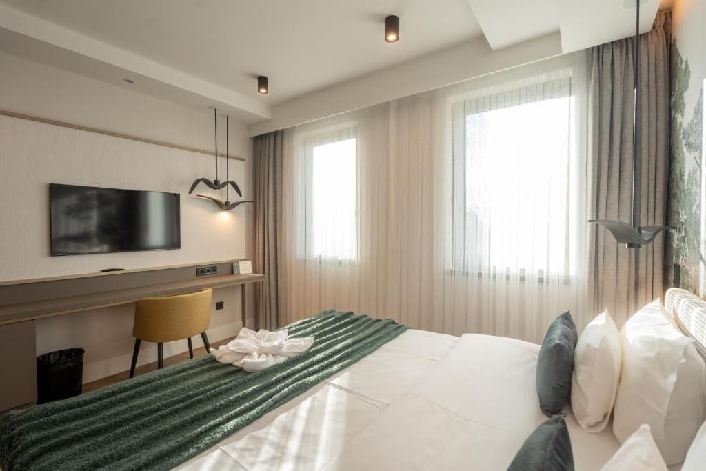 A modern hotel room with a bed, a desk, a chair, and a television.