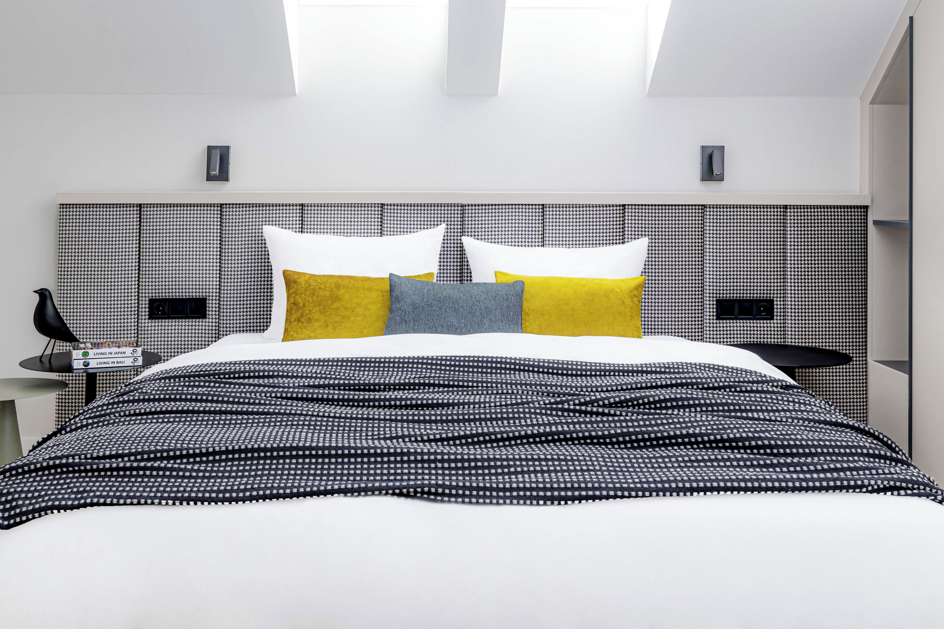 Una habitación de hotel moderna con una cama grande, un cabecero con estampado de cuadros y una mesita de noche con una lámpara.