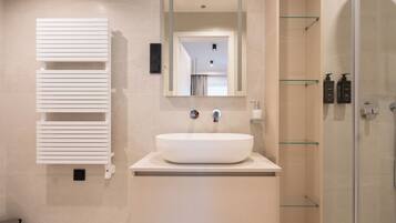 A modern bathroom with a large white sink, a mirror above it, and a glass shower enclosure.