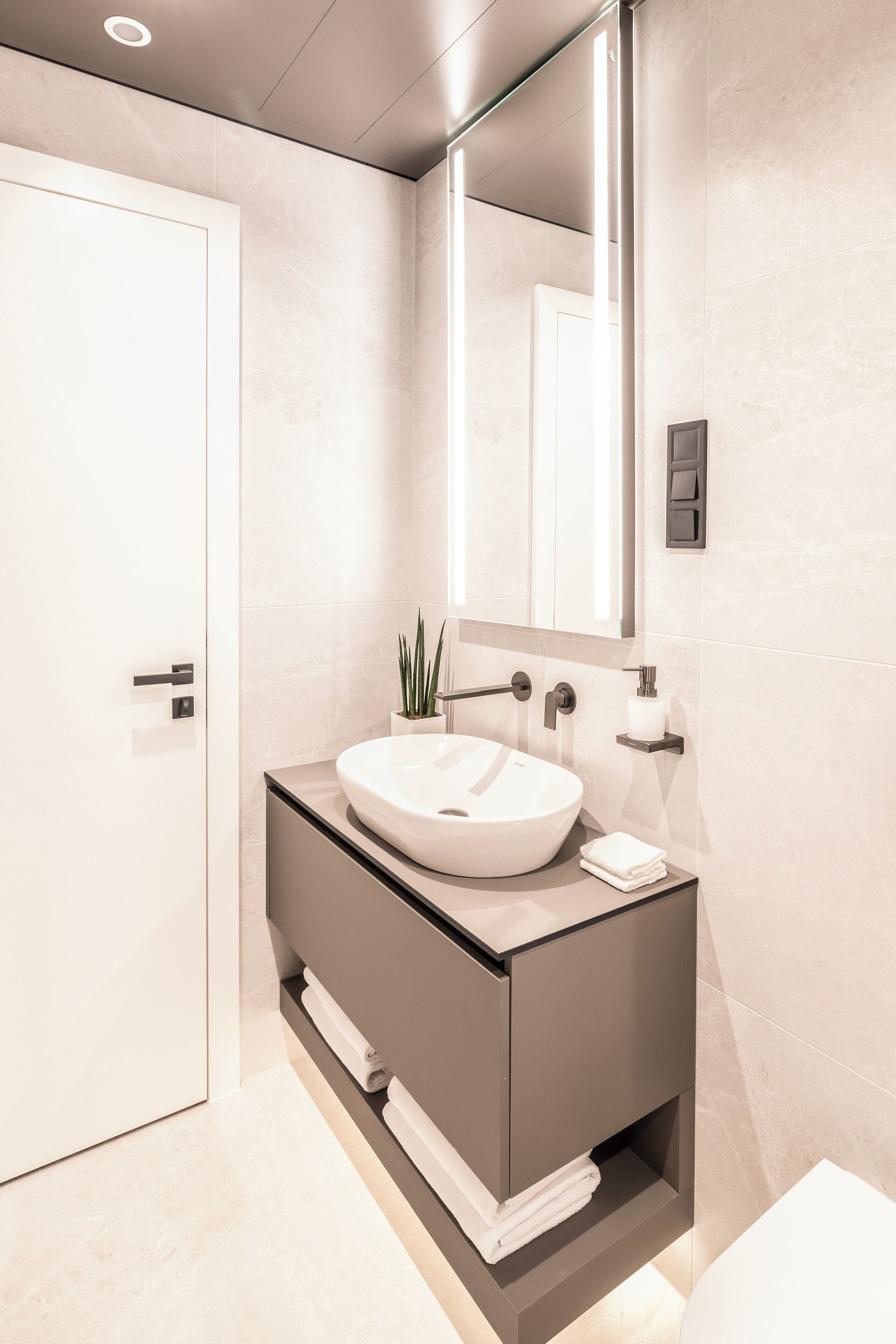 A modern bathroom with a white sink, dark vanity, and a large mirror.