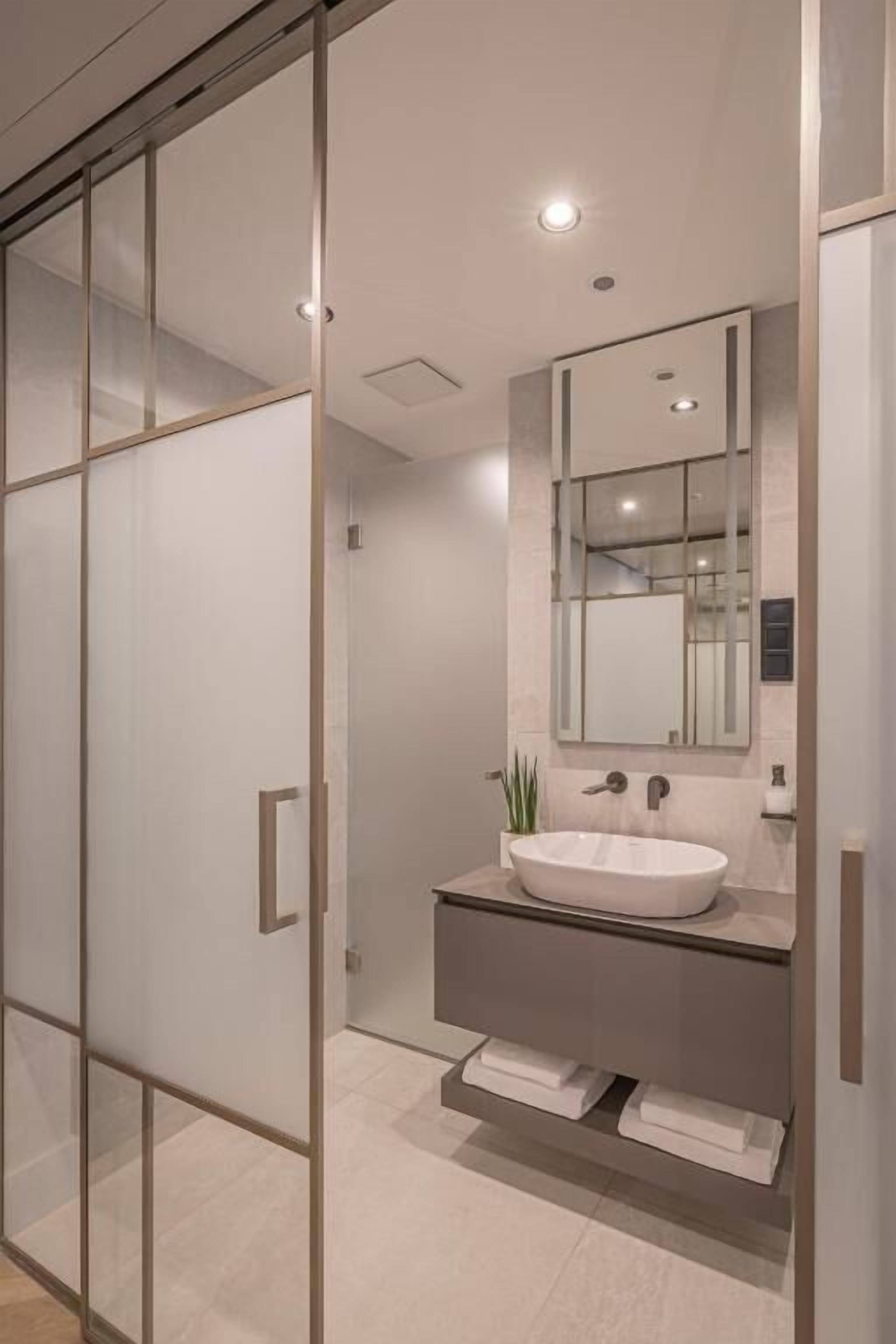 Un bagno moderno con una parete divisoria in vetro, un lavandino bianco e uno specchio sopra.