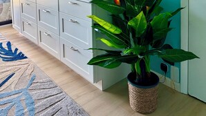 Una habitación con un armario blanco, un televisor de pantalla plana, una planta en maceta y un equipo de aire acondicionado montado en la pared.