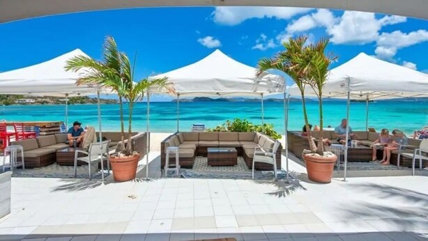 Un lounge frente a la playa con asientos al aire libre, toldos blancos y vista al océano.