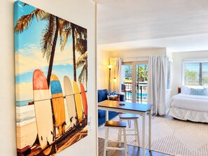 A hotel room with a beach-themed painting, a dining area, and a balcony with a view.