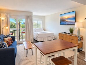 A hotel room with a bed, a sofa, a dining table, and a view of the outdoors.