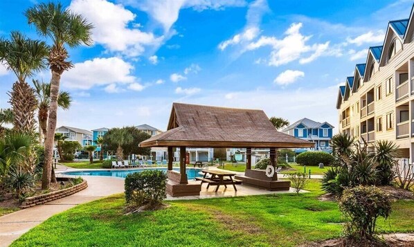 A pool area with a gazebo, palm trees, and a building with balconies.