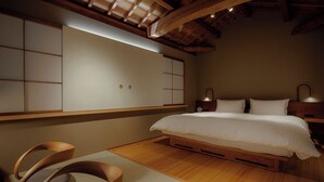 A bedroom with a wooden bed, a built-in wardrobe, and a traditional Japanese-style chair. - RYOKAN KURASHIKI Residence (Kurashiki)