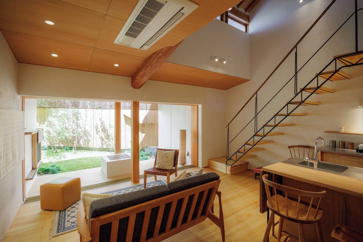 A modern interior with a wooden staircase, a kitchen area, and a seating area with a view of the outdoors.
