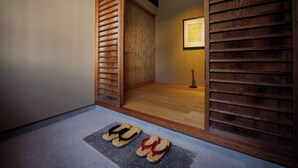 A room with a wooden floor, a sliding door, and a pair of slippers on the floor. - RYOKAN KURASHIKI Residence (Kurashiki)