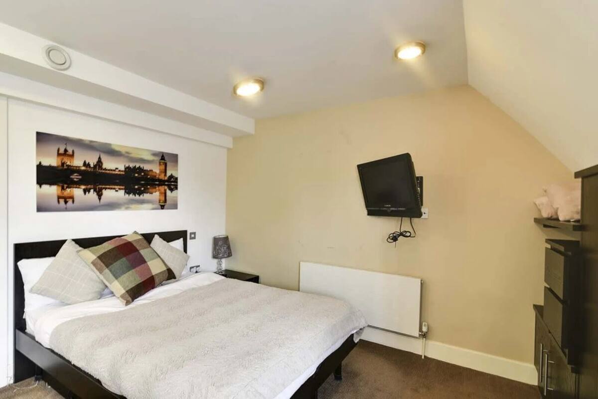 A bedroom with a bed, a TV mounted on the wall, a radiator, and a picture of a cityscape.