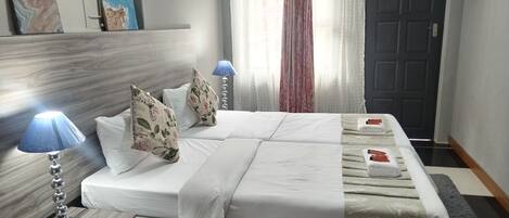 Et hotelværelse med en stor seng, to sengeborde med lamper, et vindue med let gardin og en dør.