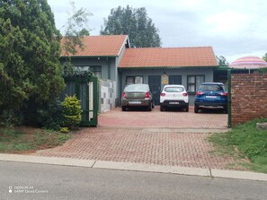 A building with a tiled roof, a brick entrance, and three parked cars. - Room-home of Peace and Tranquility (Pretoria)