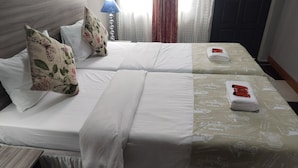 A hotel room with two beds, each with white bedding and floral-patterned pillows. There is a lamp on one side and a folded towel on the other. - Room-home of Peace and Tranquility (Pretoria)