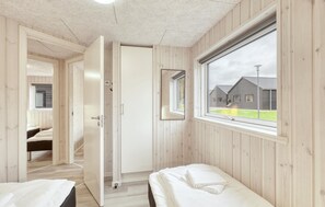 A bedroom with a wooden floor, a bed, a window, and a door leading to another room.