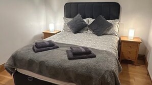 A neatly made bed with a dark headboard, two bedside tables with lamps, and a wooden floor. - Rose Cottage in Ennistymon - Near Cliffs of Moher (Magherareagh)