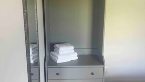 A grey wardrobe with a mirror, a hanging rack, and a stack of folded towels. - Rose Cottage in Ennistymon - Near Cliffs of Moher (Magherareagh)