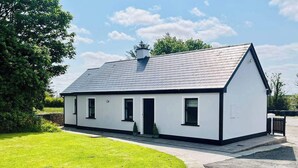 A single-story house with a sloped roof, a small porch, and a well-maintained lawn. - Rose Cottage in Ennistymon - Near Cliffs of Moher (Magherareagh)