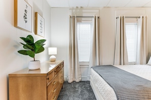 A bedroom with a bed, a dresser, a plant, and two windows with curtains. - 13 Mi to Buffalo: Cozy Apartment in Depew! (Depew)