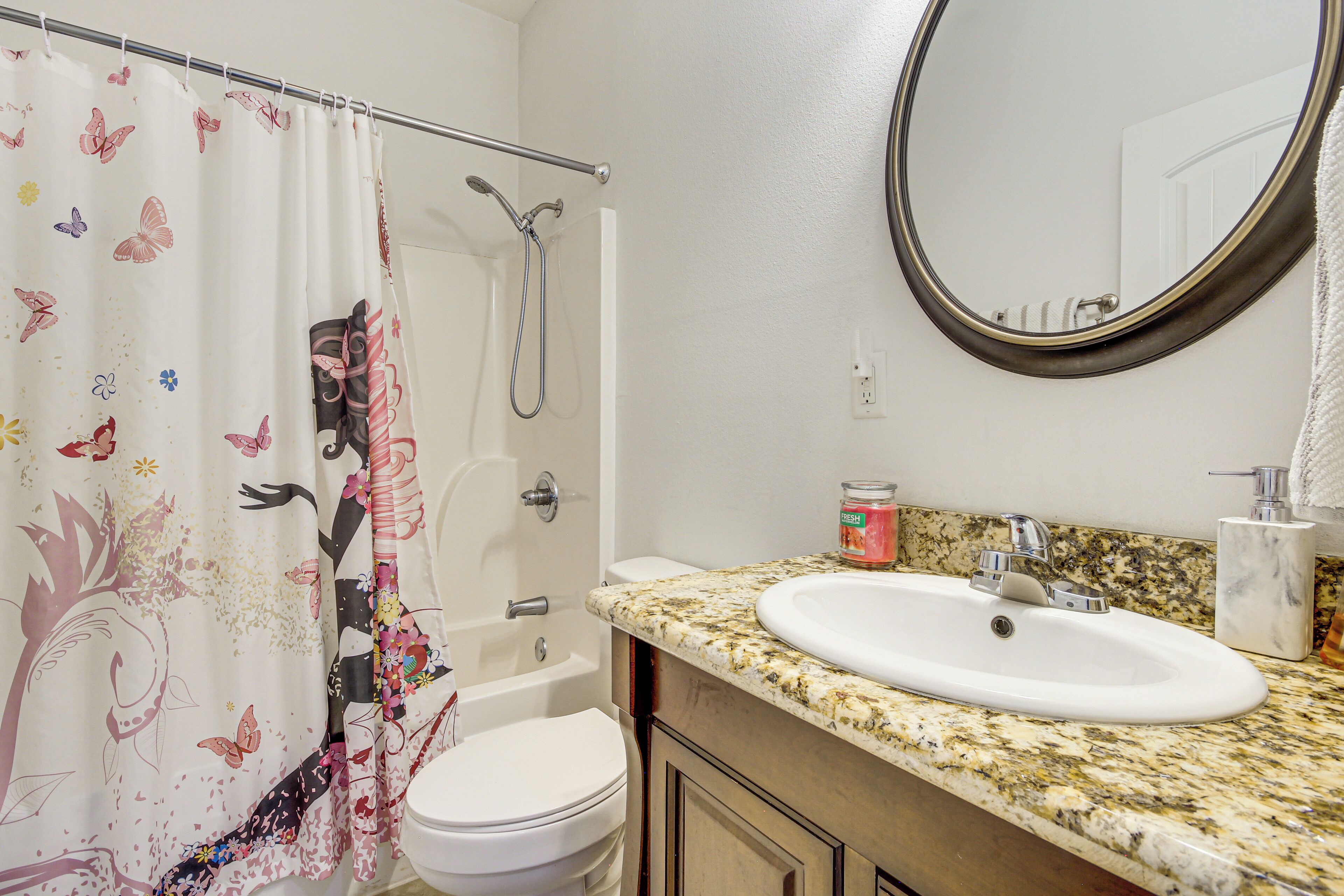 A bathroom with a shower, toilet, sink, and a mirror.