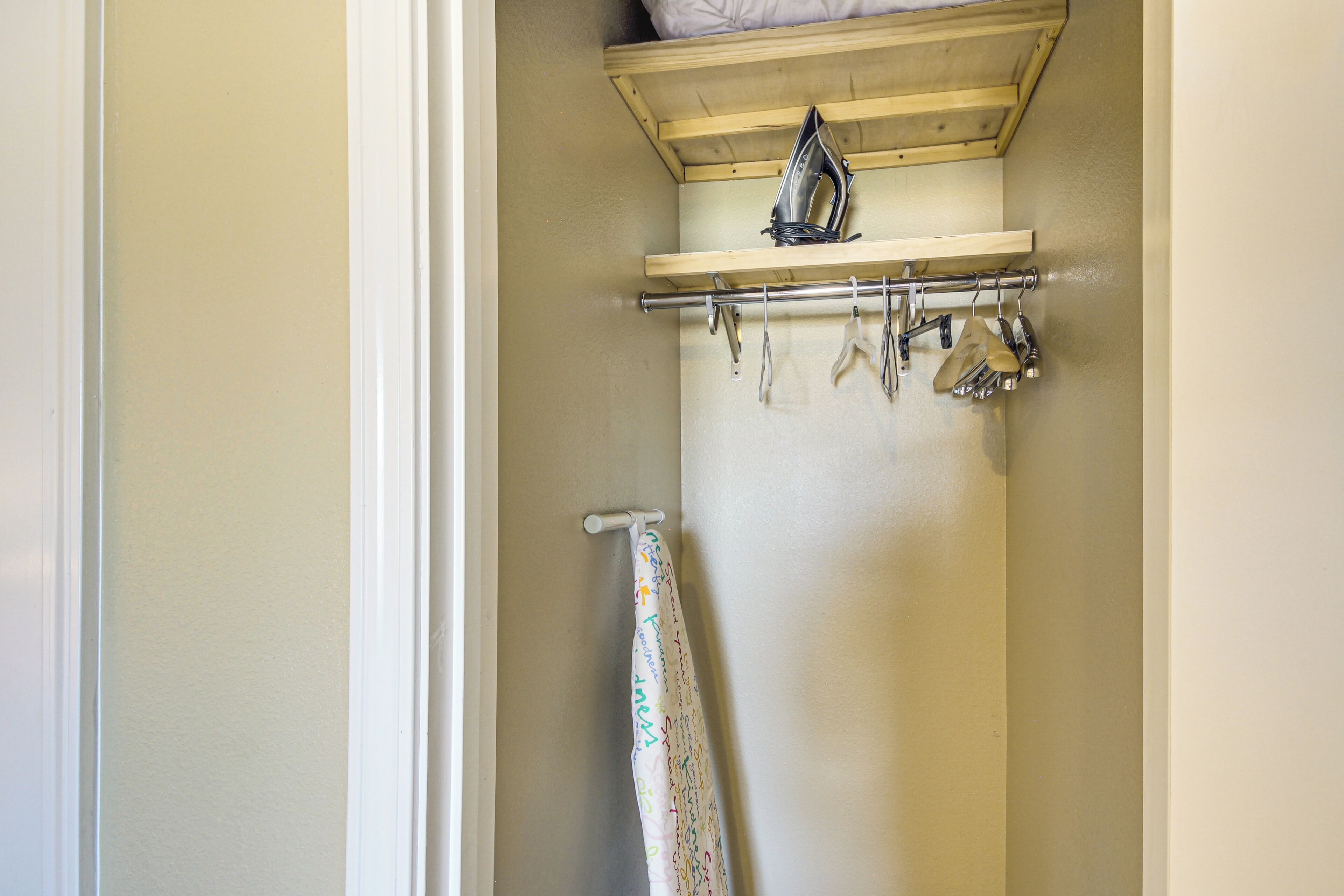 Baño con estante de madera que sostiene un planchador y toallas colgadas.