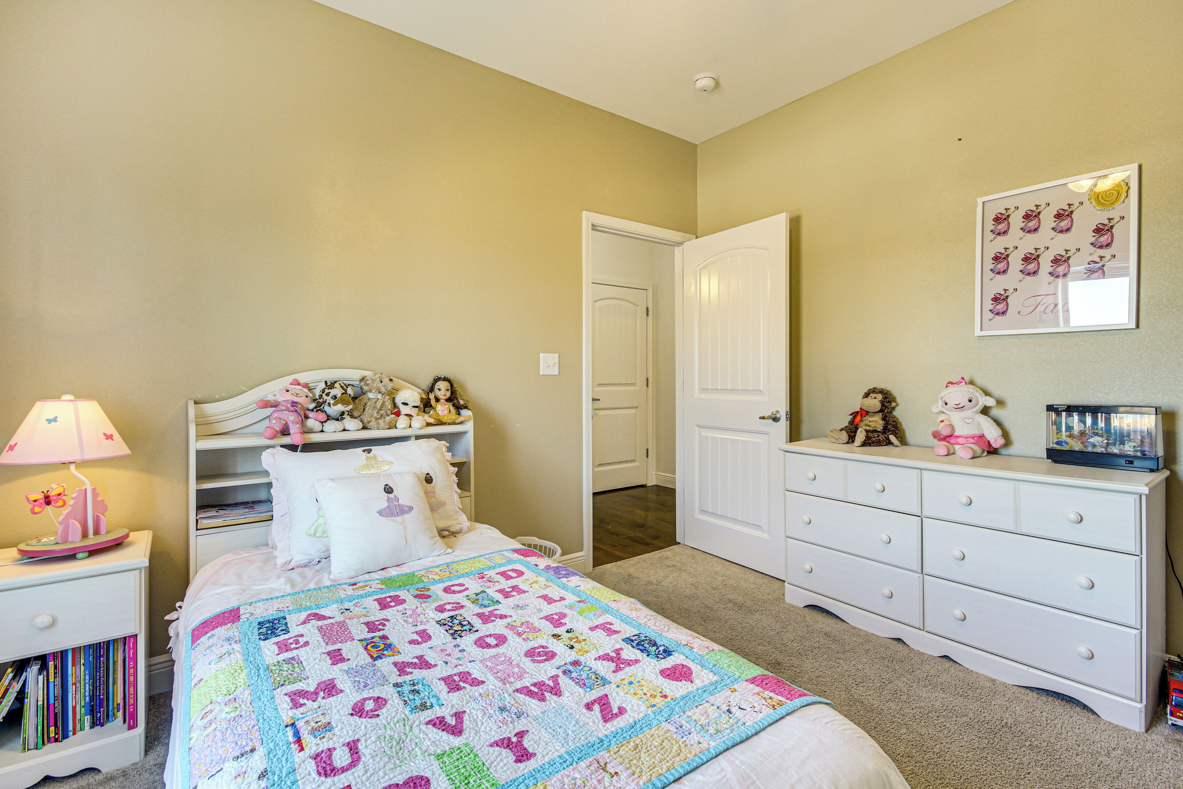 A bedroom with a bed, a nightstand, a dresser, and a door leading to another room.