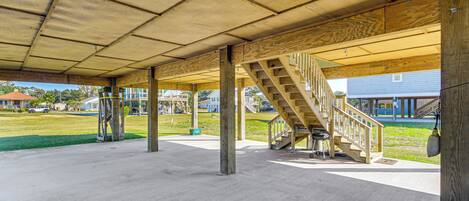 An outdoor covered area with a concrete floor, wooden beams, and a staircase leading to an upper level.