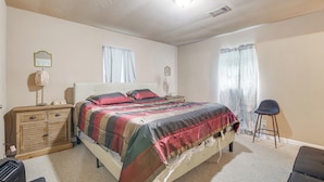 A bedroom with a bed, a nightstand, a dresser, a chair, and a window with curtains.