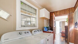 A laundry area with two white Whirlpool washers and dryers, a window with blinds, and a wooden door leading to another room.