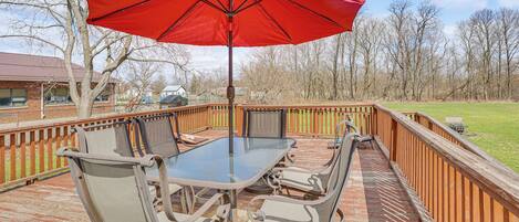 A deck with a glass table and chairs, a red umbrella, and a wooden railing.