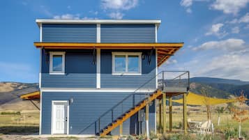 Una casa de dos pisos con balcón, escaleras y un patio con mobiliario exterior.