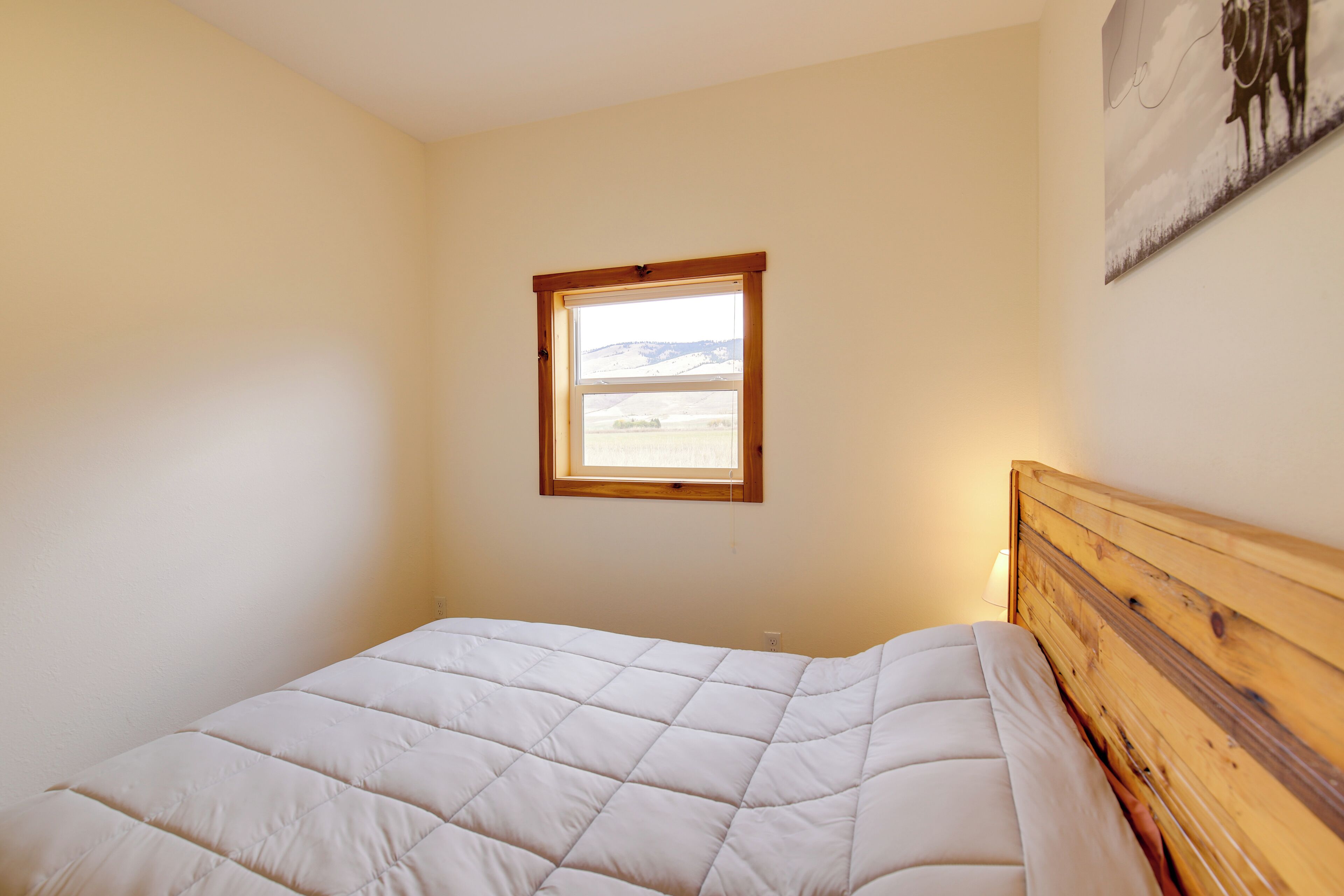 A bedroom with a wooden headboard, a window with a view of the countryside, and a wall-mounted artwork.