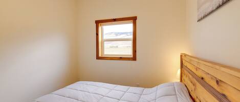A bedroom with a wooden headboard, a window with a view of the countryside, and a wall-mounted artwork.