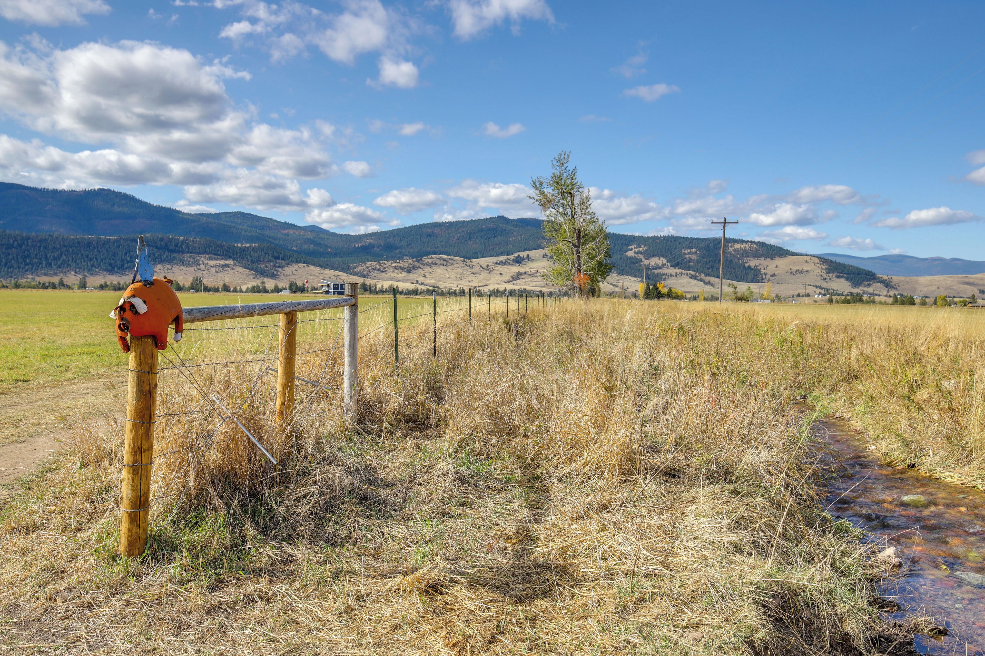 A rural landscape with a wooden fence, a metal gate, and a clear blue sky.